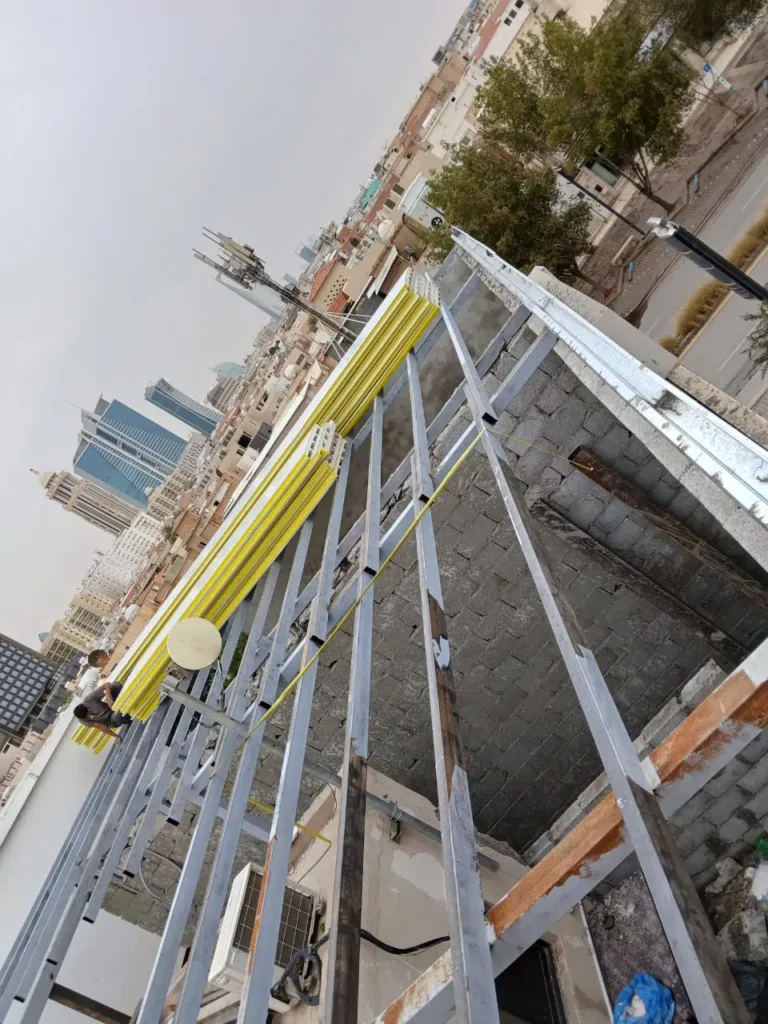 هيكل معدني ممدد فوق سطح مبنى سكني أثناء تجهيز تركيب سقف ساندوتش بانل، مع صفوف من الألواح الصفراء