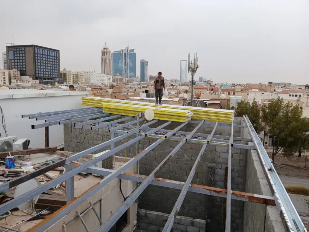 تركيب هيكل معدني لسقف ساندوتش بانل فوق مبنى في الرياض مع تجهيز الألواح قبل التثبيت