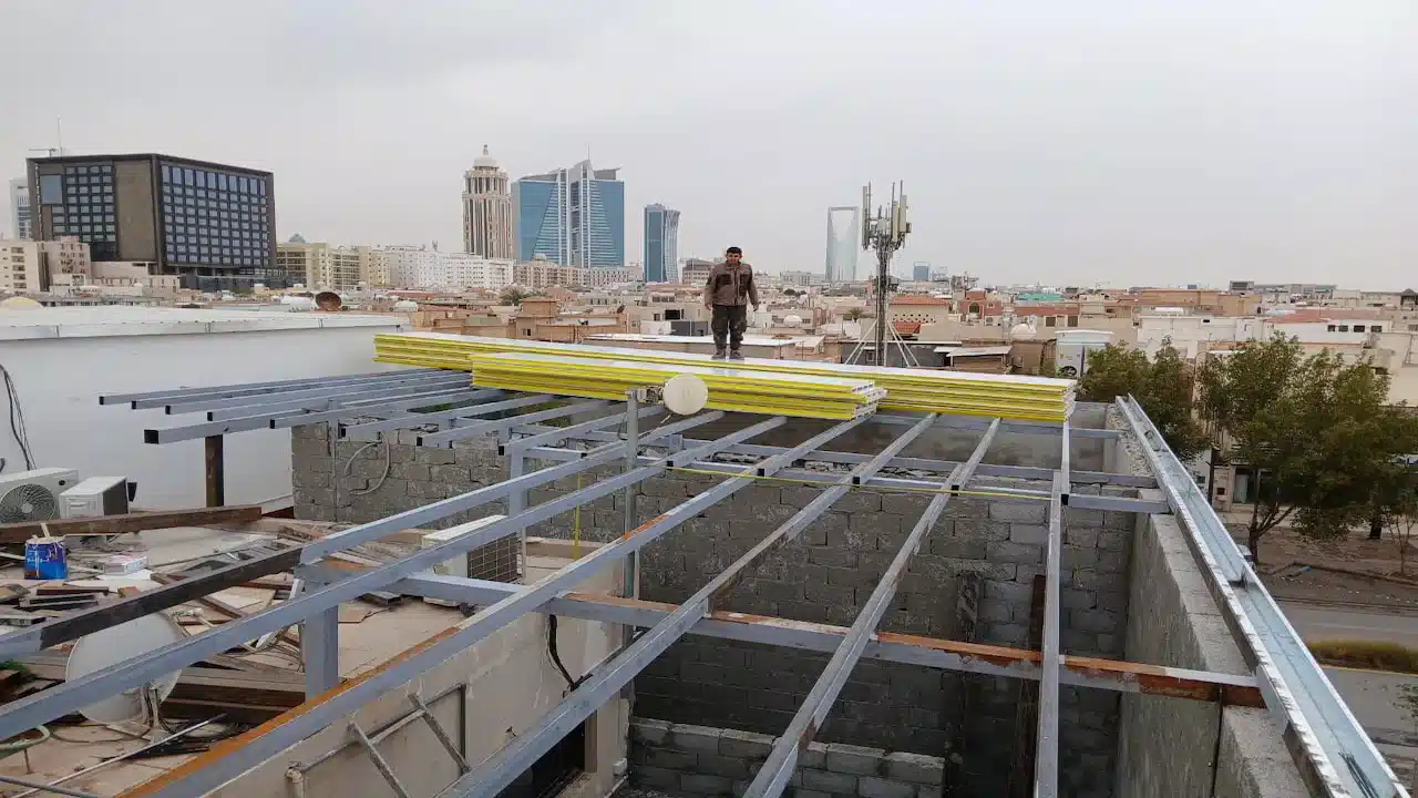 تركيب هيكل معدني لسقف ساندوتش بانل فوق مبنى في الرياض مع تجهيز الألواح قبل التثبيت